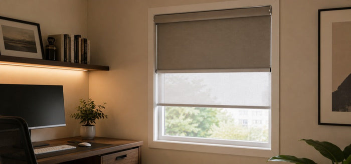 Modern home office corner with a single window featuring dual roller shades, with the blackout layer on the upper section and light-filtering fabric below.