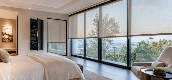 Modern bedroom with large motorized smart shades and a discreet network cabinet, showing a clean wired PoE smart home setup.