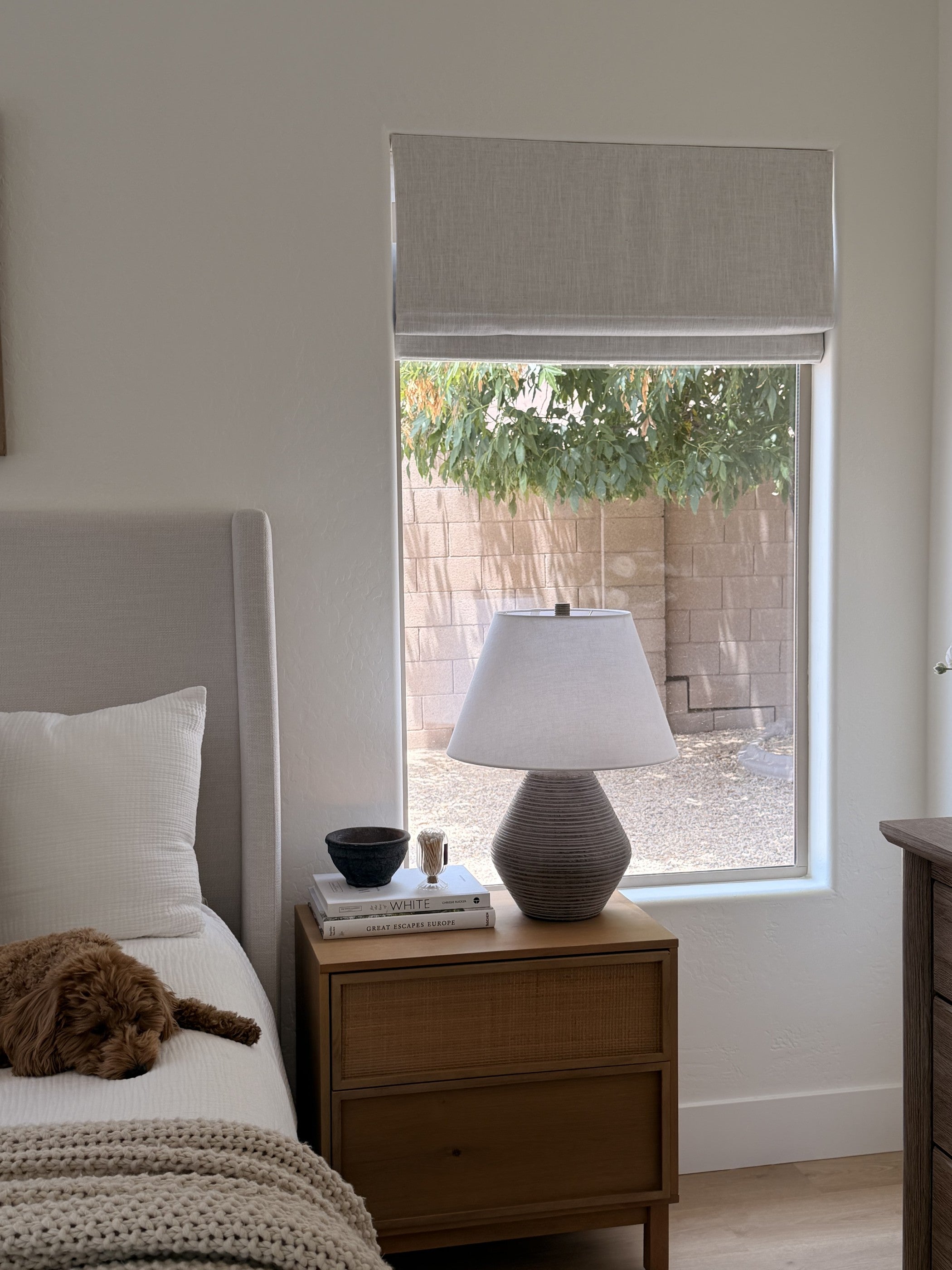 A softly lit bedroom with a motorized Roman shade partially open